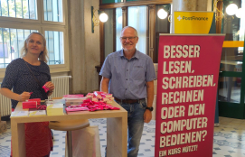 Ein Mann und eine Frau an einem Stand in der Post. Sie machen auf digitale Kompetenzen aufmerksam.