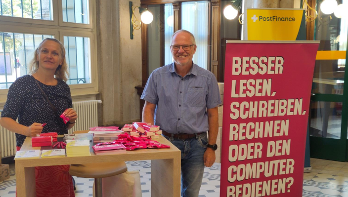 Un homme et une femme devant un présentoir à prospectus à la Poste. Ils sensibilisent le public aux compétences numériques.